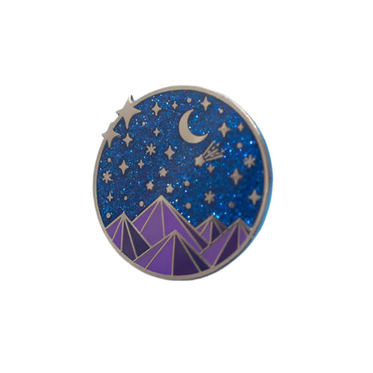 A colorful enamel pin with a fantasy court theme, featuring a starry night sky and mountains, accompanied by a butterfly clasp and placed on a blue background.