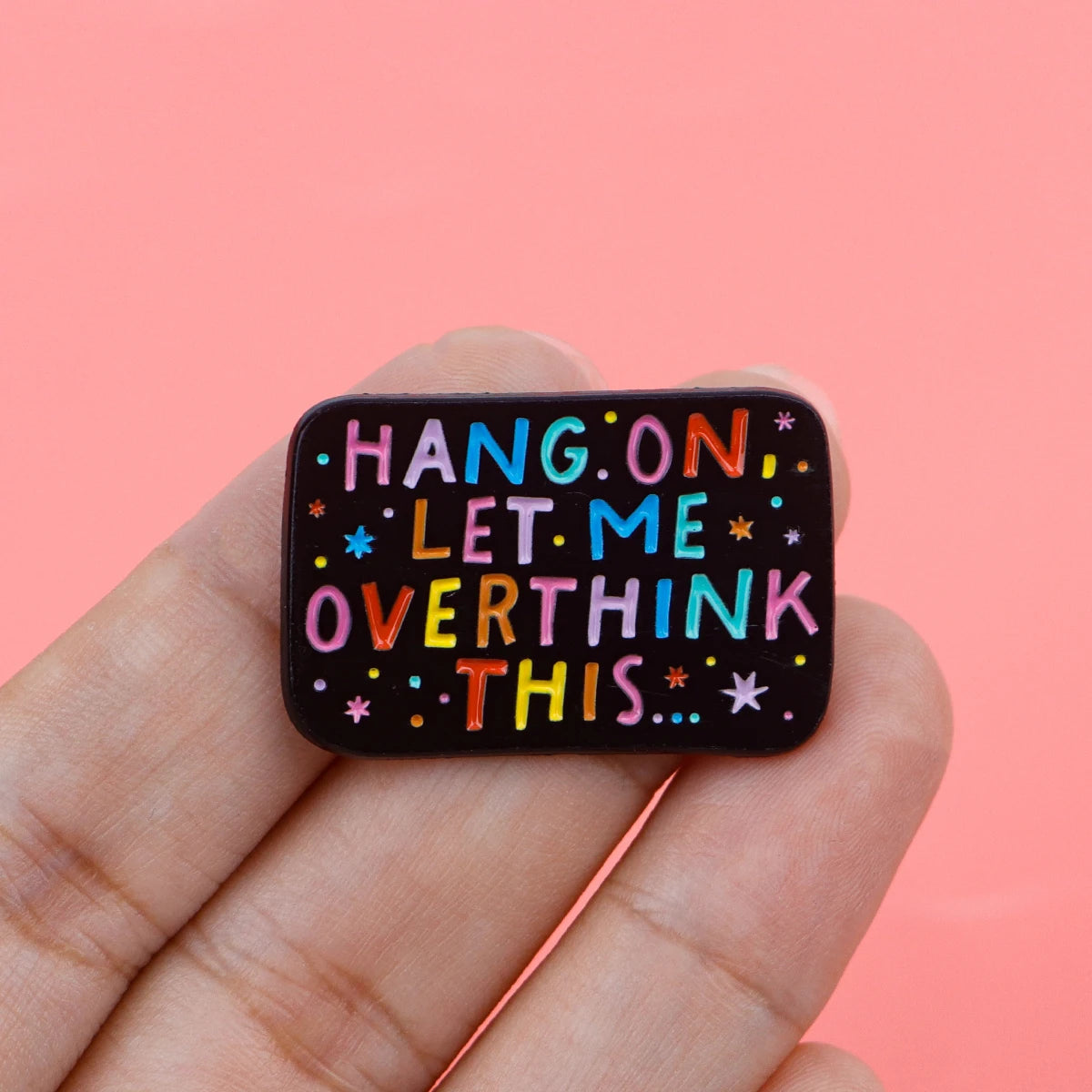 'Hang on, let me overthink this' enamel pin held between fingers