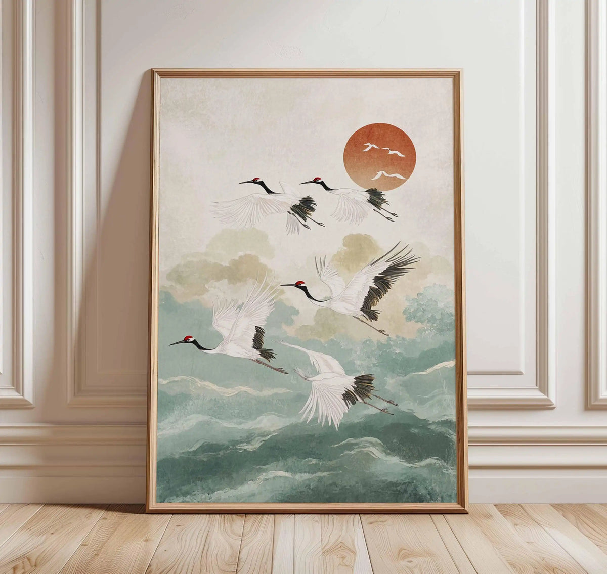 Framed artwork of cranes flying with a red sun in the background, displayed on a wall.