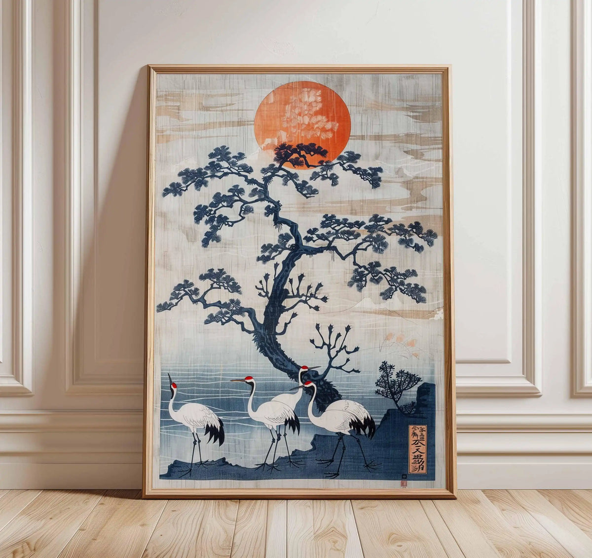 Framed artwork of cranes under a tree with a red sun on a wall.