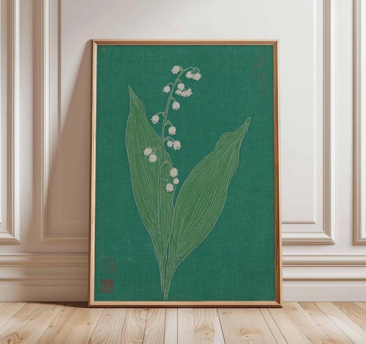 Framed botanical artwork of a plant with white flowers on a green background, leaning against a wall.