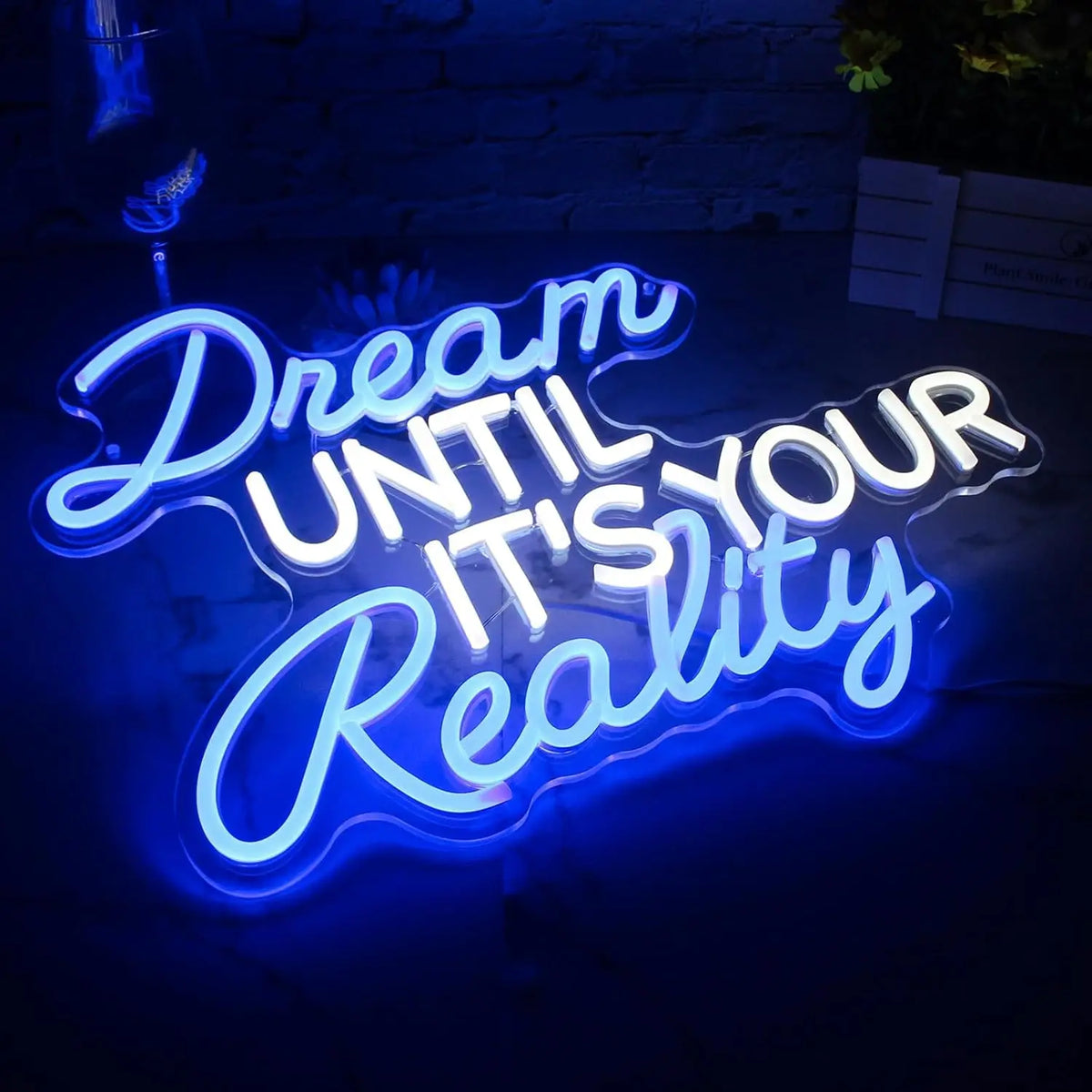 Close-up of the Dream Until It's Your Reality neon sign with blue cursive lettering and white block text