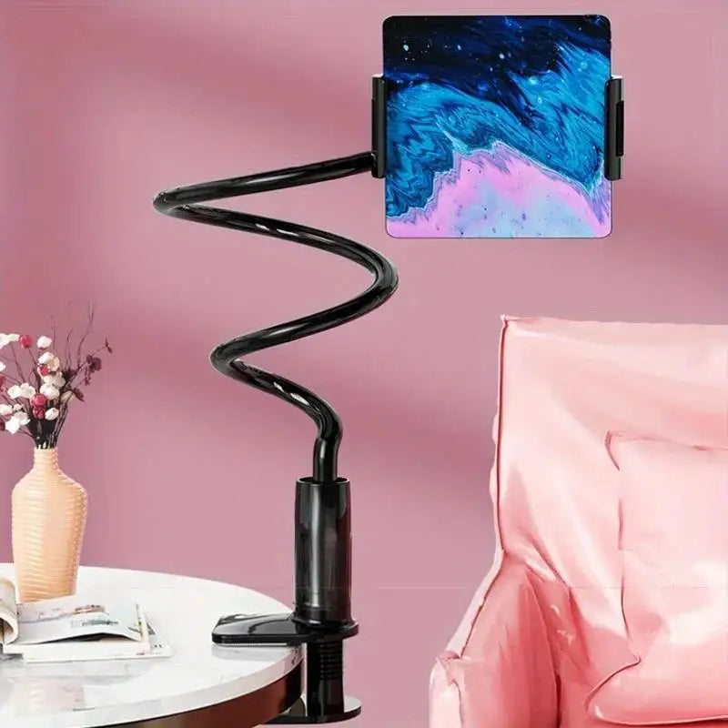 Gooseneck tablet holder clamped to a table, holding a tablet beside a pink chair