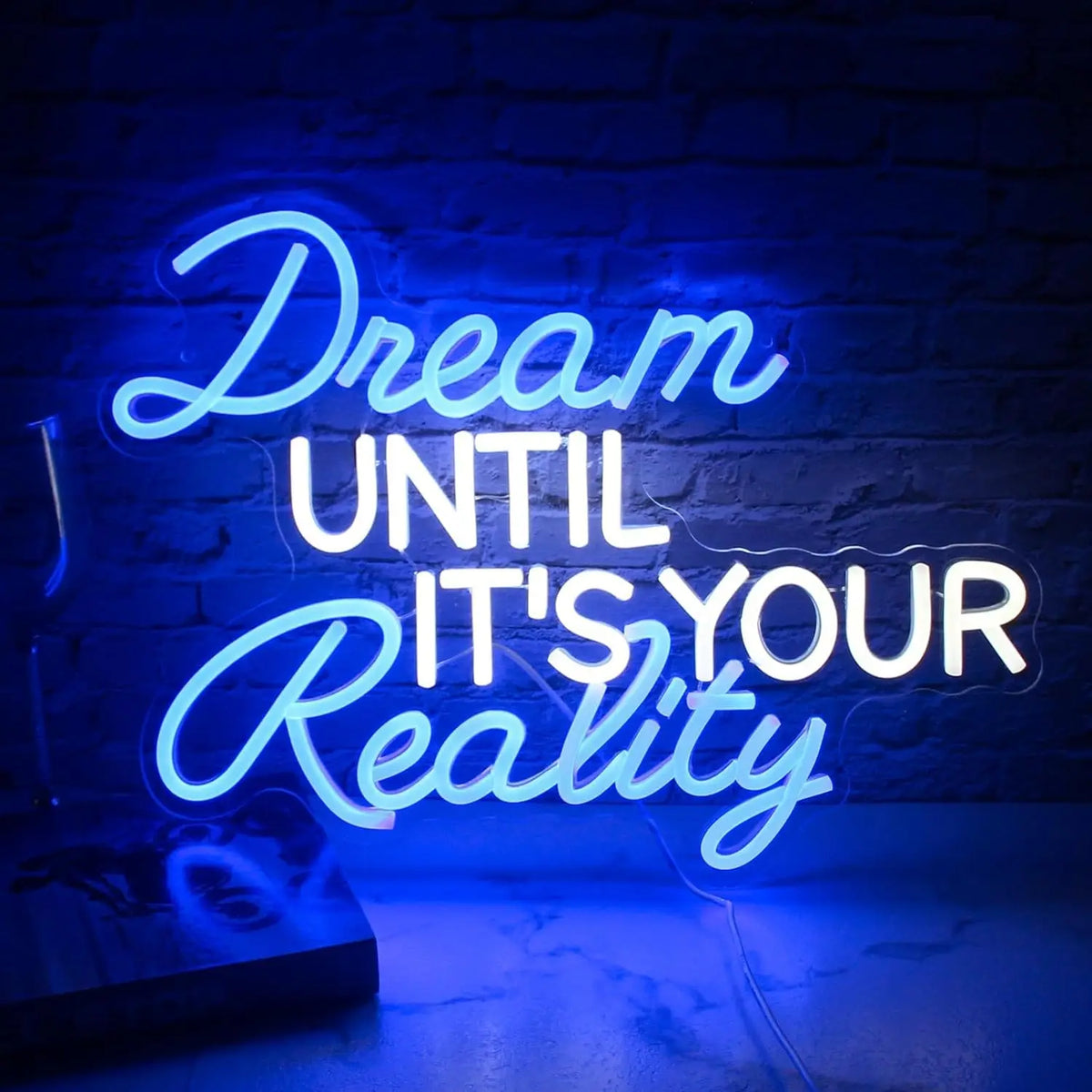 Blue and white Dream Until It's Your Reality LED neon sign displayed against a dark brick wall