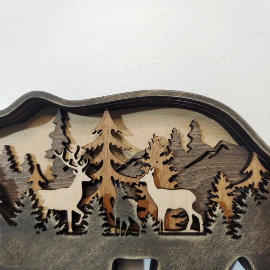 Wooden wall art with cut-out designs of deer and trees on a white background