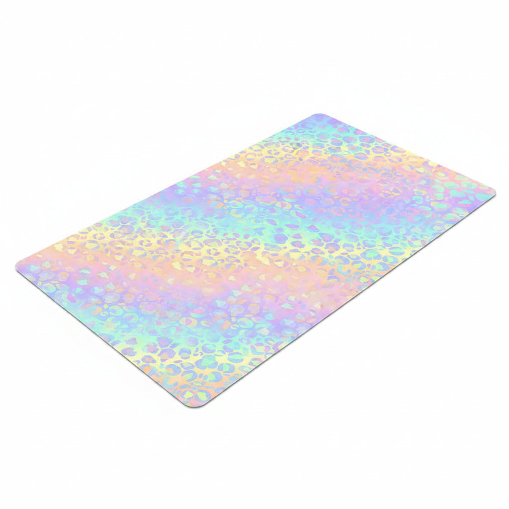 A rectangular desk mat with rounded corners, featuring a pastel rainbow leopard print pattern on a clean white background.