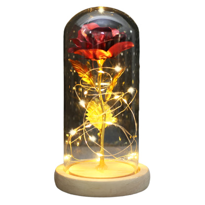 A Beauty and the Beast inspired dome light with a glass enclosure and LED lights in the shape of a rose, placed on a wooden stand.